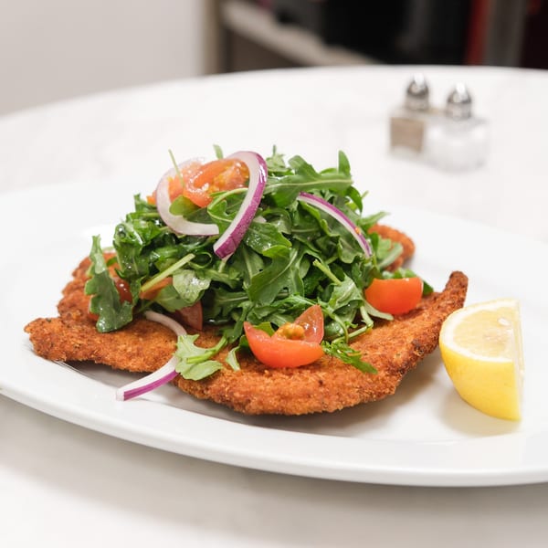 Crispy chicken cutlets topped with arugula, cherry tomatoes, red onion, and a lemon wedge.