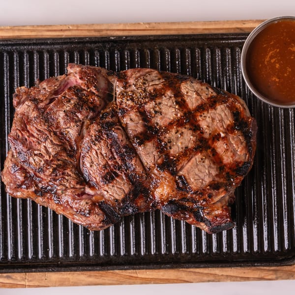 Grilled ribeye steak with grill marks and a side of sauce on a cast iron plate.