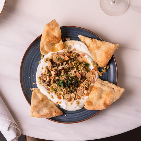 Johnny & Sanny's Italian appetizer with creamy dip, capers, almonds, and pita bread on a blue plate.