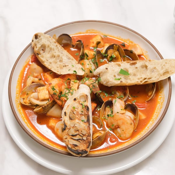 A bowl of Johnny & Sanny's Italian seafood stew with shrimp, clams, and toasted bread.