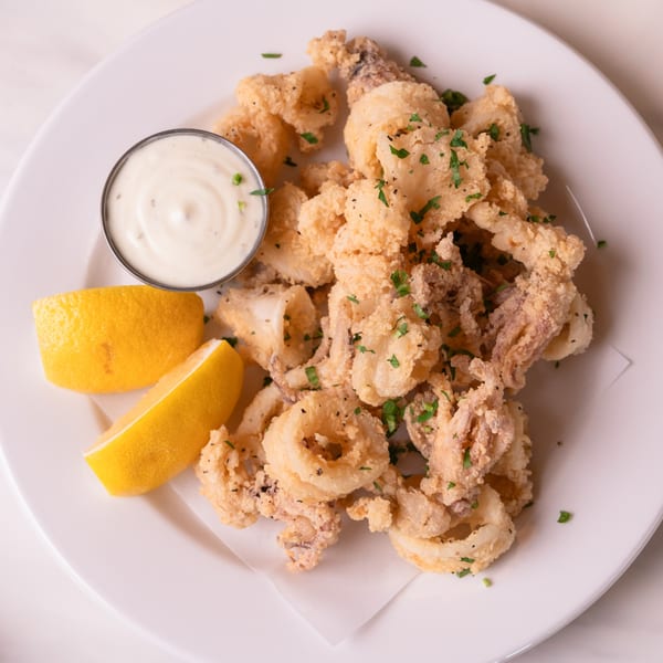 Crispy fried calamari with lemon wedges and a side of creamy dipping sauce on a white plate.