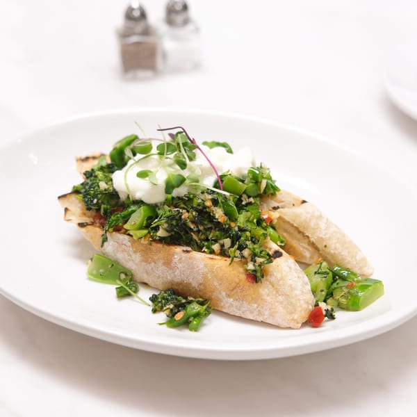 Italian bruschetta with green vegetables, white cheese, and microgreens on a white plate.