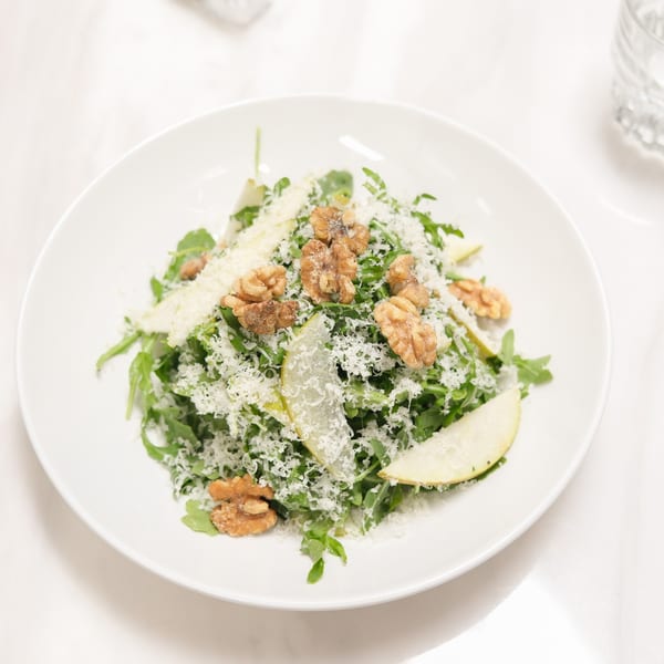 Arugula salad with shaved parmesan, pear slices, and walnuts on a white plate.